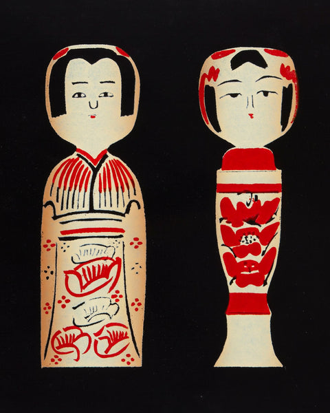 Handmade ltd edition silkscreen print with three stylized Japanese kokeshi doll figures in cream and red on a black background, photographed against a light gray wall.