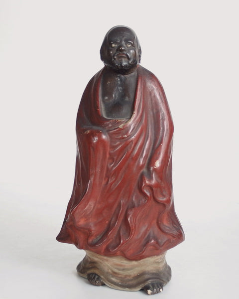 A antique standing Daruma figure with an expressive, contemplative face and beautifully flowing robes. A characterful Japanese sculpture chosen for its quiet presence.