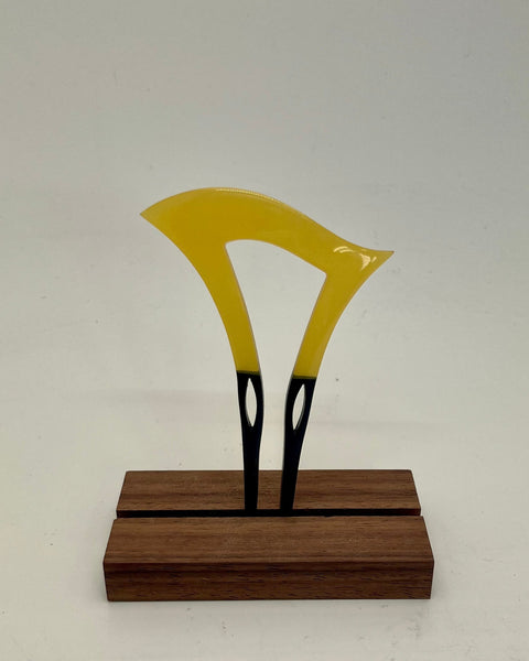 A yellow and black decorative object mounted on a rectangular dark wood base, photographed against a plain light gray background.