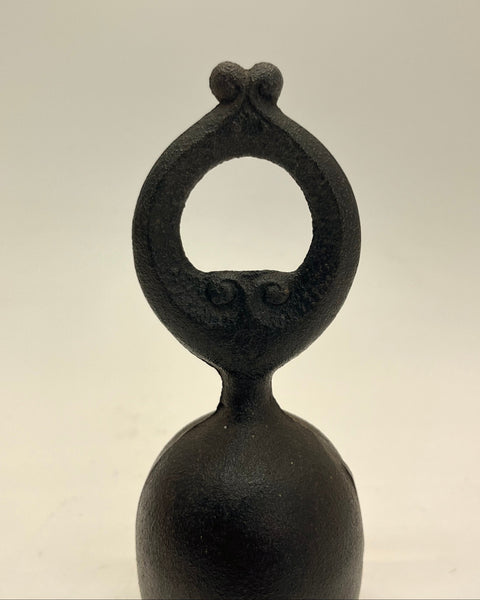 A small black cast iron bell, owl pattern with a decorative loop handle, shown against a plain light gray background.